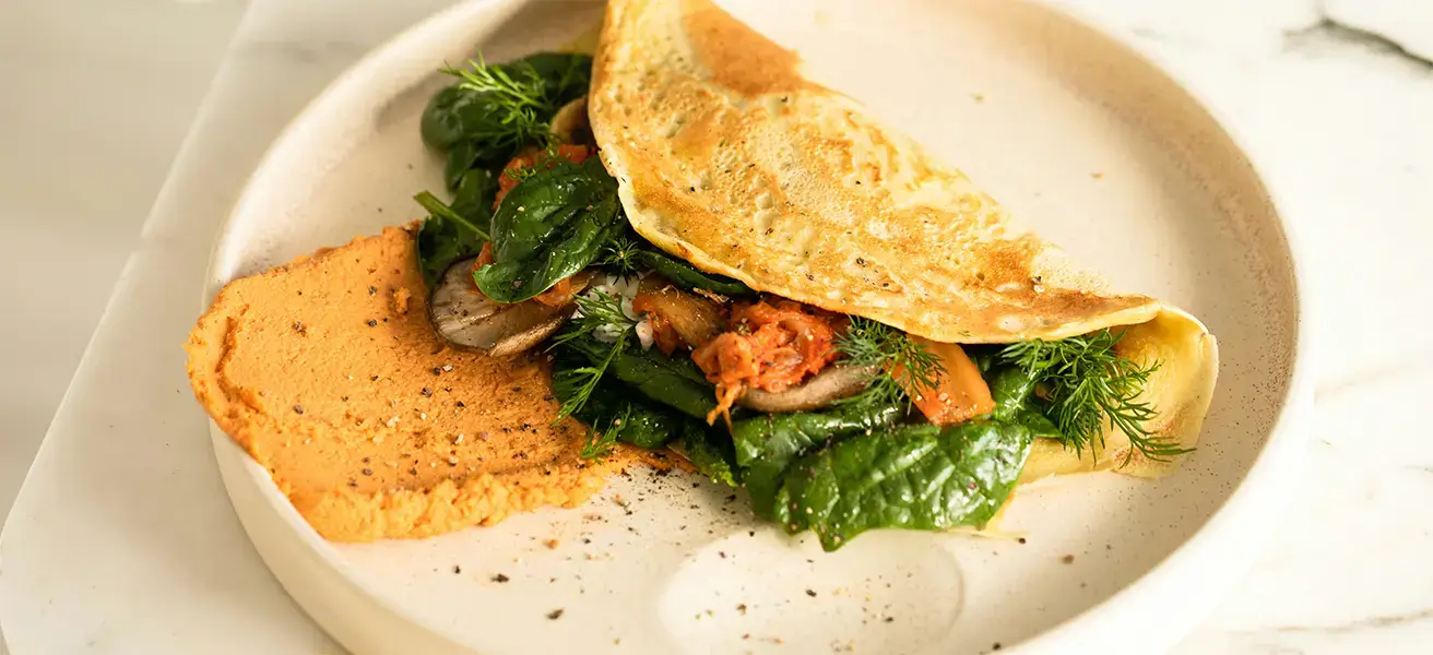 A White plate with an omelet and a side of bread. The omlet has meat and green vegetables inside.